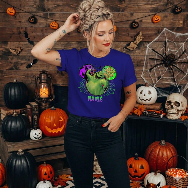 May include: A royal blue short-sleeve t-shirt featuring a graphic of the character Oogie Boogie from The Nightmare Before Christmas, surrounded by a spiderweb, a purple haunted house circle, and the text "Oogie Boogie Bash" and "NAME".