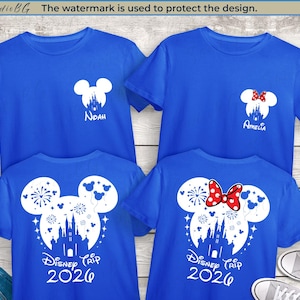 Peut inclure: Quatre t-shirts bleus avec des motifs graphiques blancs. Deux chemises pr&eacute;sentent une t&ecirc;te de Mickey Mouse avec une silhouette de ch&acirc;teau et le texte "Disney Trip 2026". Les deux autres chemises ont une t&ecirc;te de Mickey Mouse avec les noms "Noah" et "Amelia".