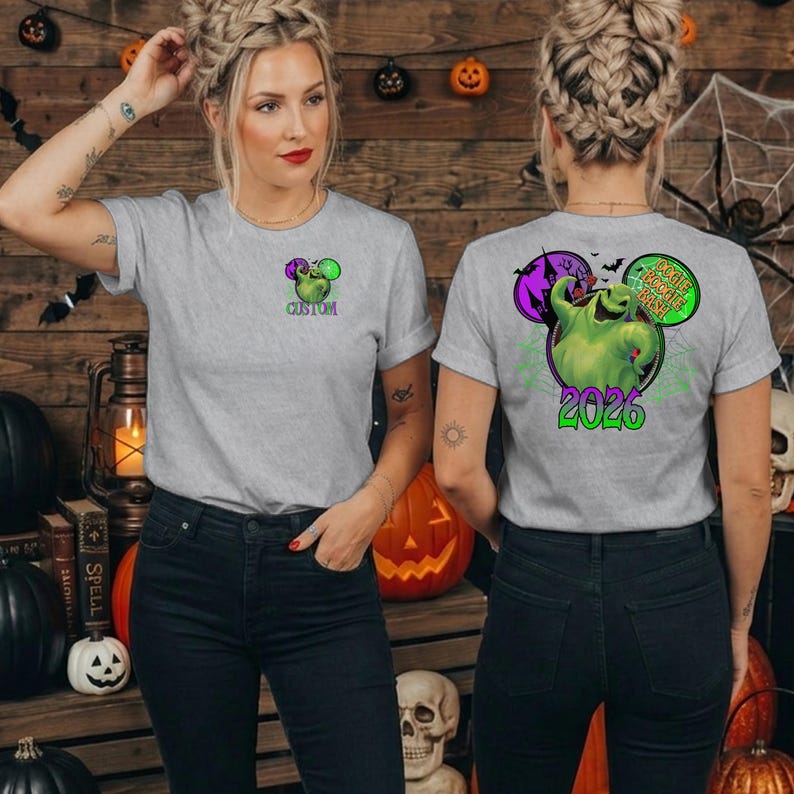 Puede incluir: Una camiseta gris claro con un peque&ntilde;o gr&aacute;fico verde del personaje Oogie Boogie en el pecho izquierdo. La parte posterior muestra un gr&aacute;fico grande de Oogie Boogie, una casa embrujada, murci&eacute;lagos y el texto Oogie Boogie Bash 2026 en morado y verde.