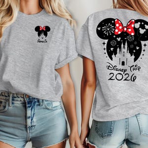 Peut inclure: T-shirt gris clair avec un motif Minnie Mouse avec un n&oelig;ud rouge et le nom "Amelia" sur le devant. Le dos du t-shirt pr&eacute;sente un motif Minnie Mouse plus grand avec un ch&acirc;teau, des feux d'artifice et le texte "Disney Trip 2026".