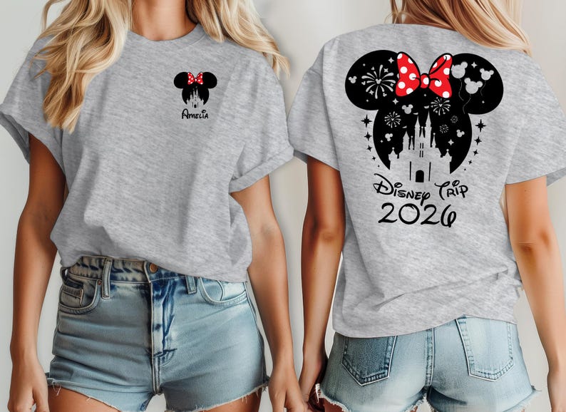 Peut inclure: T-shirt gris clair avec un motif Minnie Mouse avec un n&oelig;ud rouge et le nom "Amelia" sur le devant. Le dos du t-shirt pr&eacute;sente un motif Minnie Mouse plus grand avec un ch&acirc;teau, des feux d'artifice et le texte "Disney Trip 2026".