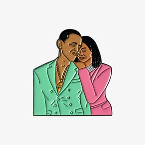 Könnte beinhalten: Eine grüne und rosafarbene Emaille-Anstecknadel mit einem Cartoon-Porträt eines Paares. Der Mann trägt einen grünen Anzug und eine goldene Kette. Die Frau trägt ein rosa Kleid und hat ihren Arm um die Schulter des Mannes gelegt.