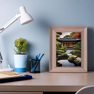 May include: A framed print of a Japanese garden with a pond, stone pathway, and a traditional wooden building. The print is in a light wood frame and is hanging on a light blue wall.