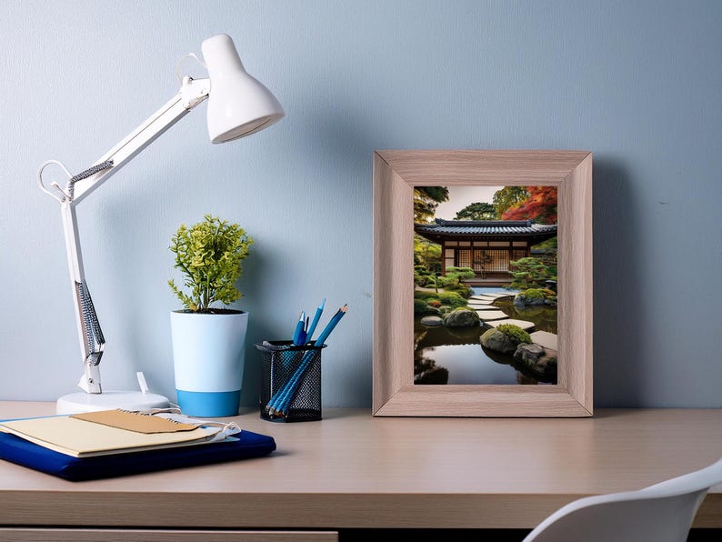 May include: A framed print of a Japanese garden with a pond, stone pathway, and a traditional wooden building. The print is in a light wood frame and is hanging on a light blue wall.