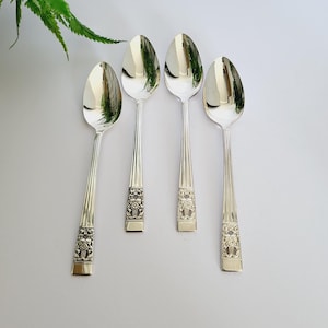 Puede incluir: Cuatro cucharas plateadas con diseños florales ornamentados en los mangos. Las cucharas tienen una superficie pulida y reflectante, dispuestas sobre un fondo blanco. Un juego de cubiertos clásico.