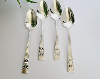 Puede incluir: Cuatro cucharas plateadas con diseños florales ornamentados en los mangos. Las cucharas tienen una superficie pulida y reflectante, dispuestas sobre un fondo blanco. Un juego de cubiertos clásico.