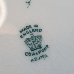 May include: Close-up of a white ceramic surface with a cracked glaze. The image features a green stamp that reads "MADE IN ENGLAND" above a crown and the word "COALPORT A.D. 1750."