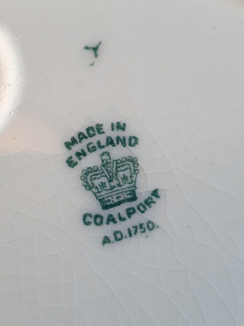 May include: Close-up of a white ceramic surface with a cracked glaze. The image features a green stamp that reads "MADE IN ENGLAND" above a crown and the word "COALPORT A.D. 1750."