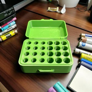 May include: A bright green battery organizer, open to display multiple circular compartments. The case is rectangular with a hinged lid. Various batteries are visible around the organizer, suggesting its use for storing and organizing batteries of different sizes.