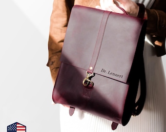 May include: A burgundy leather backpack with a flap closure and gold-colored hardware. The backpack has a top handle and adjustable straps. The text "Dr. Lennert" is visible on the front. The bag is held by a person.