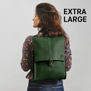 A woman with long brown hair is wearing a floral shirt and carrying a green backpack.