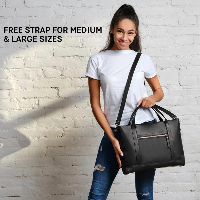A young woman in a white t-shirt and jeans is holding a black leather tote bag and smiling at the camera.