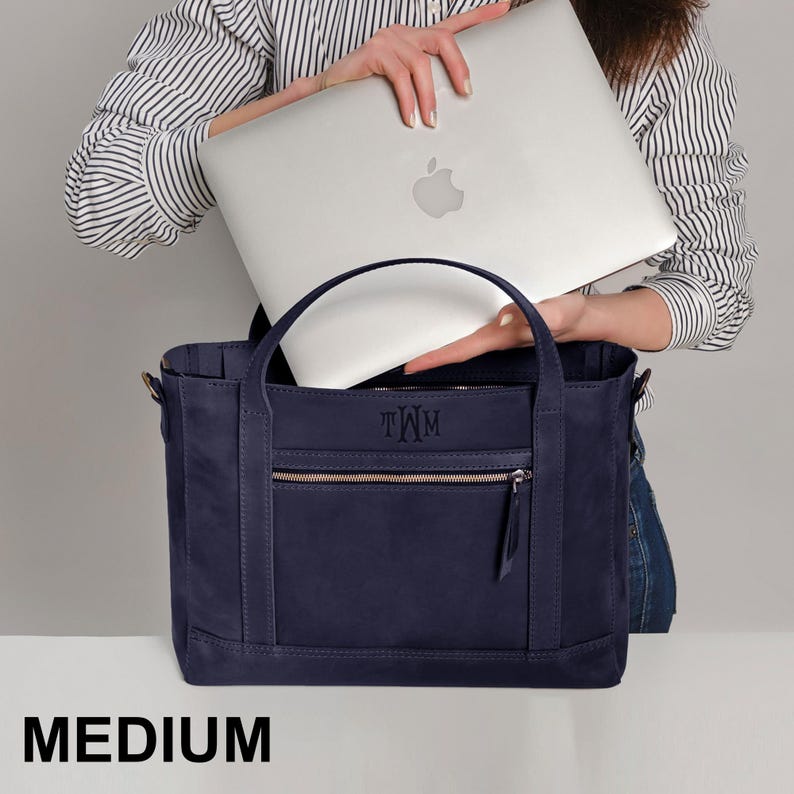 A woman holding a laptop and a medium-sized navy blue handbag.