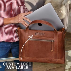 A person holding a brown leather tote bag with a laptop inside, and there is a logo on the bag.
