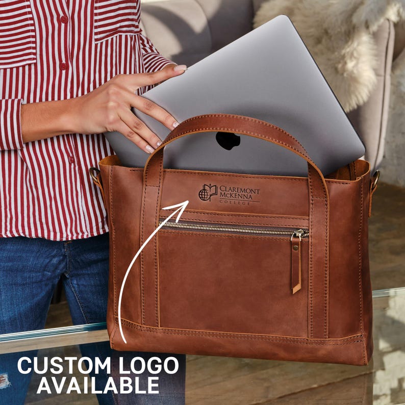 A person holding a brown leather tote bag with a laptop inside, and there is a logo on the bag.