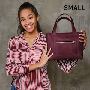 A young woman in a red and white striped shirt is holding a burgundy handbag with a personalized monogrammed logo.