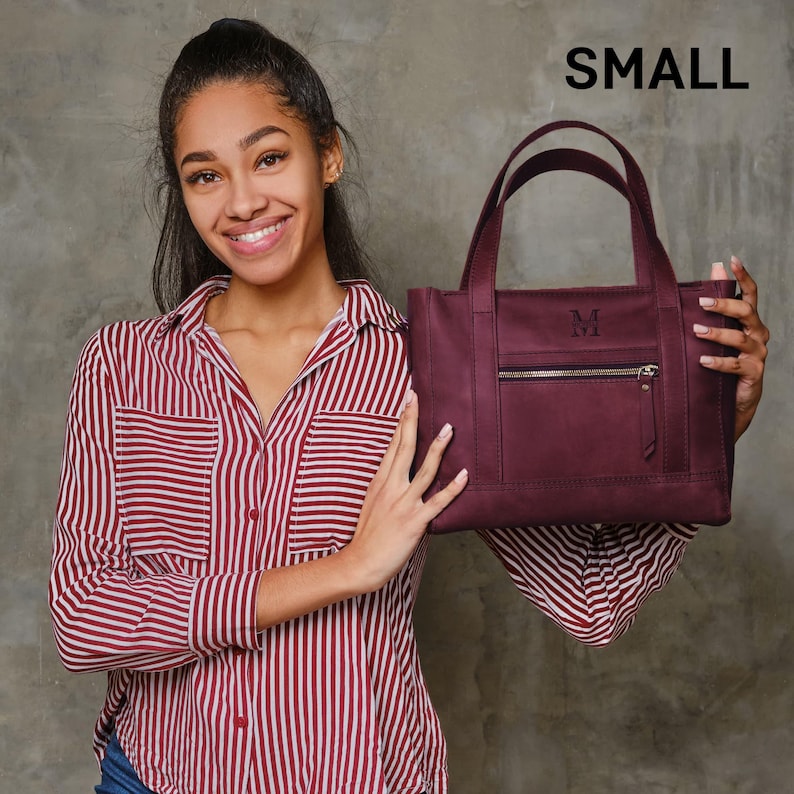 A young woman in a red and white striped shirt is holding a burgundy handbag with a personalized monogrammed logo.
