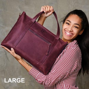 A woman is holding a large burgundy leather handbag and smiling.
