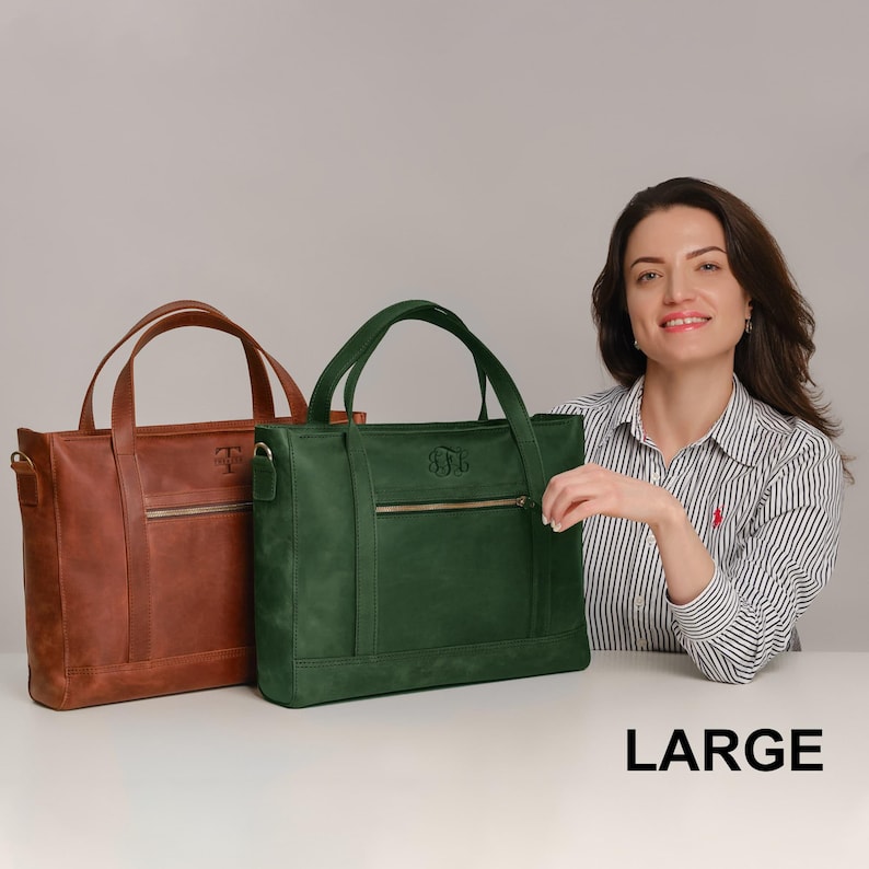 A woman is sitting at a table with two large leather handbags in front of her.