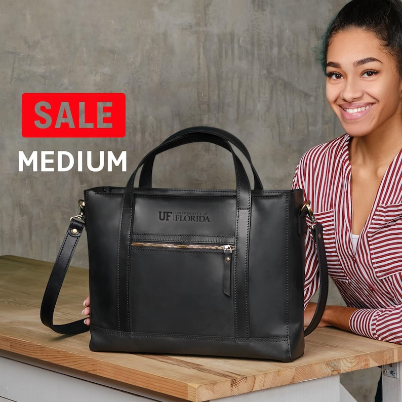 A woman is smiling and posing next to a black leather tote bag with the University of Florida logo on it.
