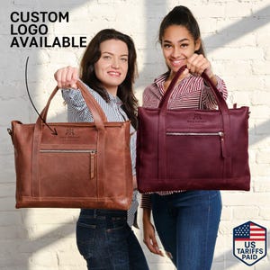 Peut inclure: Deux sacs fourre-tout en cuir, un marron et un bordeaux, sont présentés. Chaque sac a une poignée supérieure, une poche avant zippée et un logo "Mary Johnson Realtors". Le texte "CUSTOM LOGO AVAILABLE" est également visible.