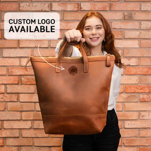 a woman holding a brown leather handbag in front of a brick wall