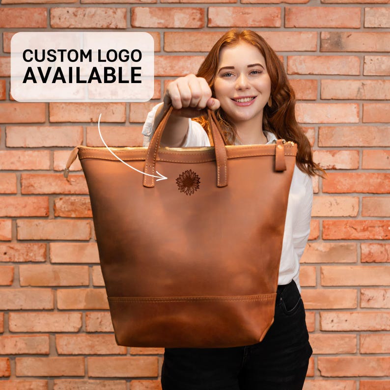 a woman holding a brown leather handbag in front of a brick wall