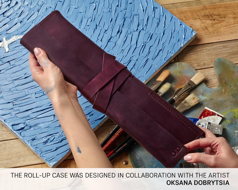 Peut inclure: Un &eacute;tui enroulable en cuir bordeaux pour fournitures artistiques. L'&eacute;tui est enroul&eacute; et attach&eacute; avec une sangle en cuir bordeaux. L'&eacute;tui est con&ccedil;u en collaboration avec l'artiste Oksana Dobrytsya.
