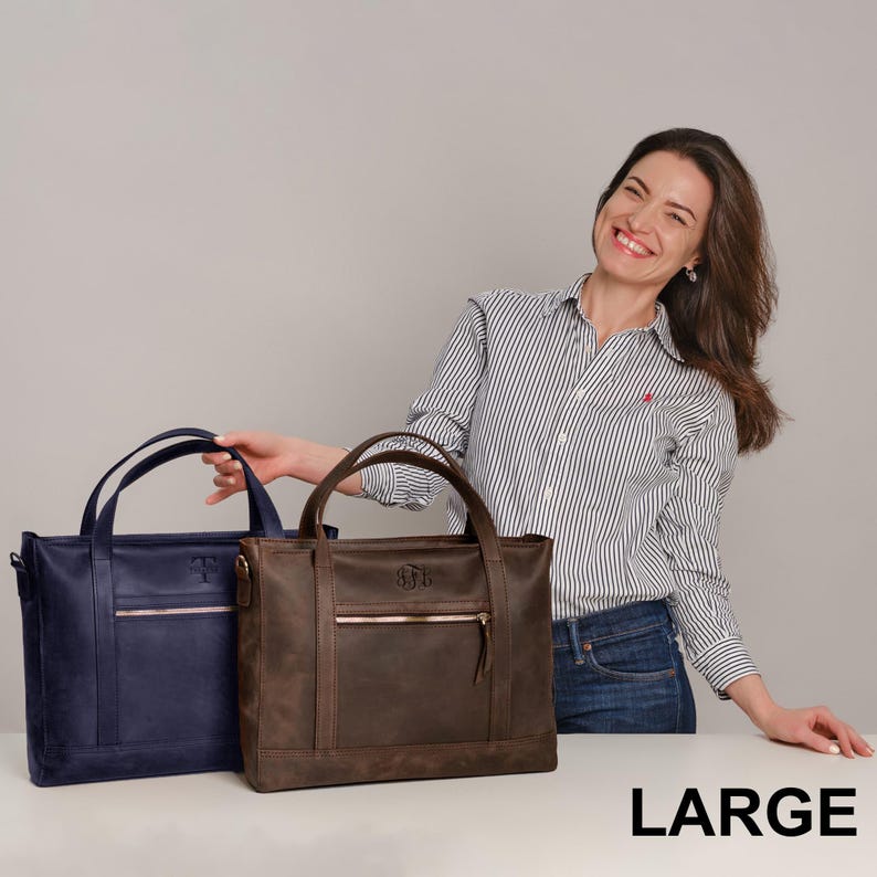 A woman is standing next to two large leather handbags, smiling and posing for the camera.