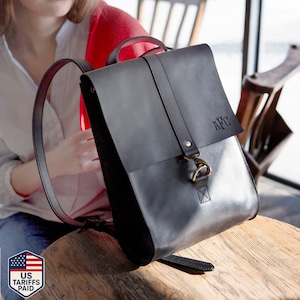 A black leather backpack with the initials "AFC" on it, placed on a wooden surface.