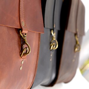 A close-up view of three leather bags, each with a metal clasp and zipper, hanging side by side.