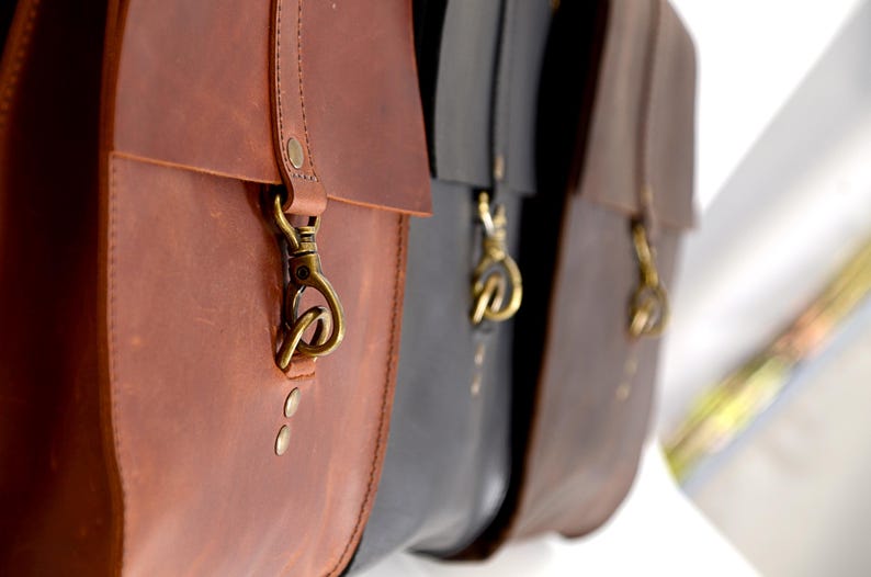 A close-up view of three leather bags, each with a metal clasp and zipper, hanging side by side.