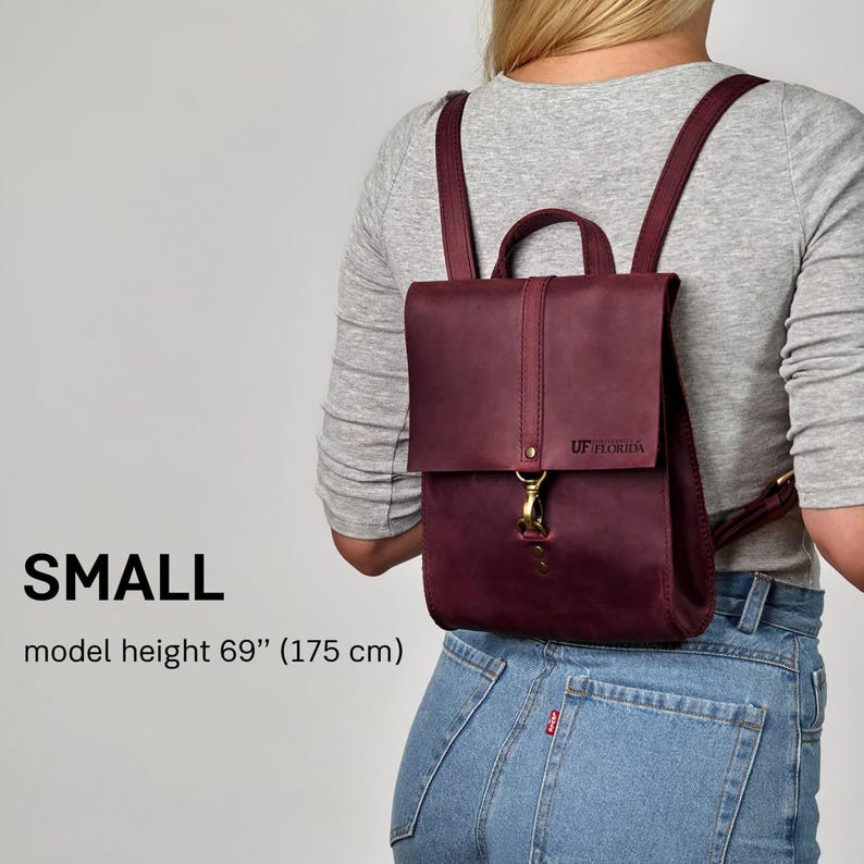 A person wearing a maroon backpack and a gray shirt, with the backpack size indicated as small.