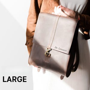A person is holding a large leather backpack with the name "Dr. Lennert" printed on it.