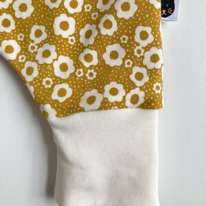 May include: Mustard yellow fabric with a white floral pattern. The fabric has a white ribbed cuff.