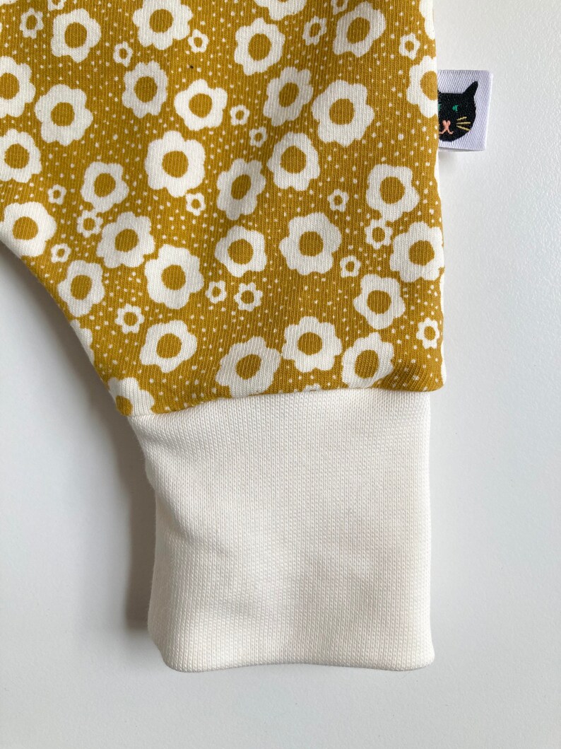 May include: Mustard yellow fabric with a white floral pattern. The fabric has a white ribbed cuff.