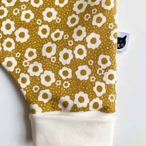 May include: Mustard yellow fabric with a white floral pattern. The fabric has a white cuff at the bottom and a black cat logo patch on the right side.