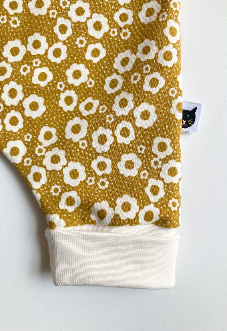 May include: Mustard yellow fabric with a white floral pattern. The fabric has a white cuff at the bottom and a black cat logo patch on the right side.