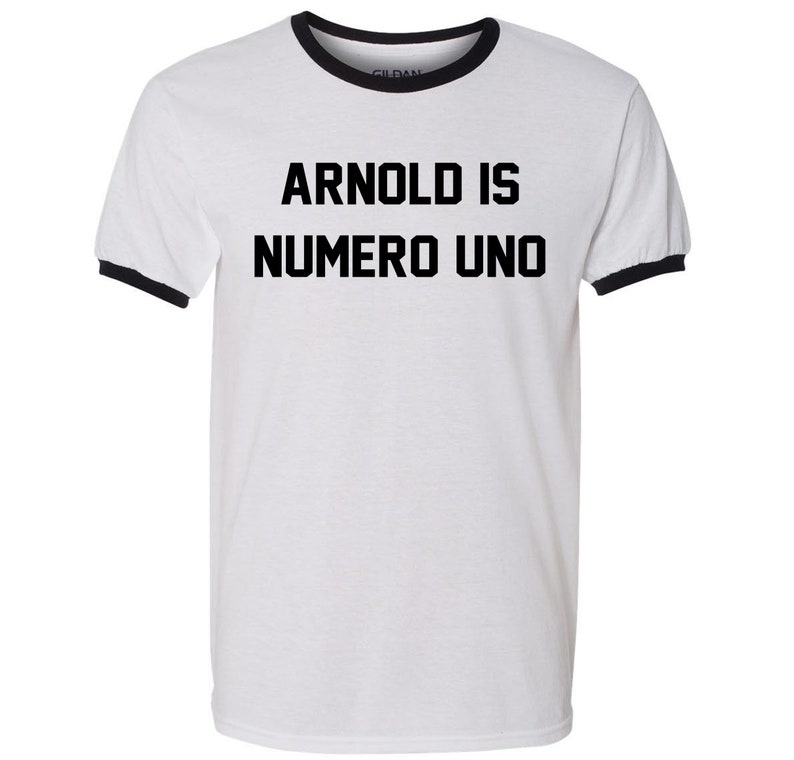 May include: White t-shirt with a black ringer and the text "ARNOLD IS NUMERO UNO" printed in black.
