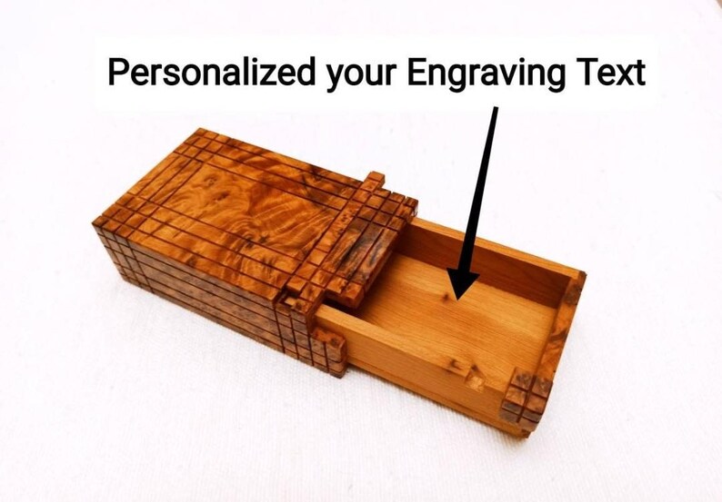 May include: A rectangular wooden box with a sliding drawer mechanism. The exterior features a dark brown wood grain with a grid-like pattern. The interior is a lighter natural wood tone. Text above reads: Personalized your Engraving Text.