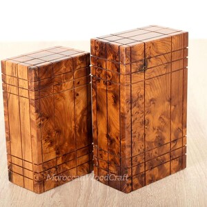 May include: Two rectangular wooden boxes with a natural brown wood grain pattern. Each box features a grid of vertical and horizontal grooves carved into the surface, creating a segmented appearance. The text MoroccanWoodCraft is visible.