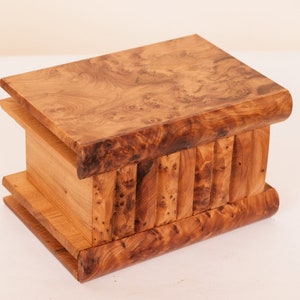 Könnte beinhalten: Eine Holzkiste mit einem einzigartigen, ineinandergreifenden Design. Die Kiste ist aus hellbraunem Holz mit einer natürlichen Maserung.