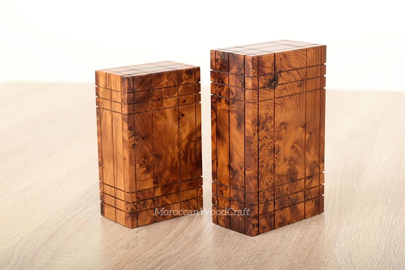 May include: Two rectangular wooden boxes with a natural brown burl wood grain pattern. Each box features a grid of horizontal and vertical grooves carved into the surface. The text Moroccan WoodCraft is visible on the lower front of the boxes.