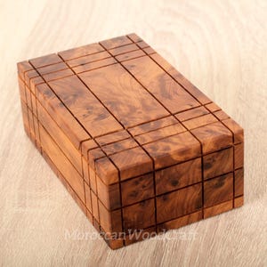 May include: A rectangular wooden box featuring a natural brown burl wood grain pattern. The exterior surface is divided into a grid of small, recessed square and rectangular sections, creating a textured, geometric appearance across the top and sides.