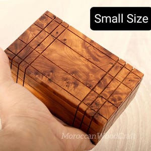 May include: A rectangular wooden puzzle box with a natural brown grain pattern and visible grid-like grooves on the surface. The box features a black rectangular label with the white text Small Size and a watermark reading MoroccanWoodCraft.