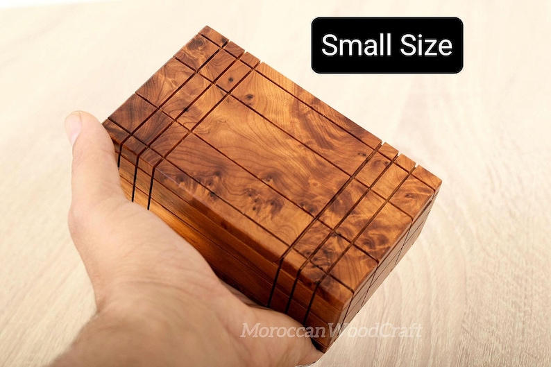 May include: A rectangular wooden puzzle box with a natural brown grain pattern and visible grid-like grooves on the surface. The box features a black rectangular label with the white text Small Size and a watermark reading MoroccanWoodCraft.