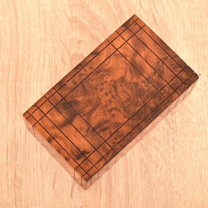 Peut inclure: Une boîte rectangulaire en bois de couleur brun foncé. Le couvercle et les côtés présentent un motif incrusté, et le grain naturel du bois est visible. La boîte est probablement destinée au rangement ou à l'exposition, environ 15 cm de long.
