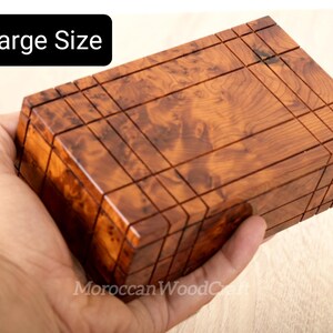 May include: A rectangular wooden box with a polished finish and a distinct burl wood grain pattern. The surface features a grid of incised lines creating a geometric design. A black label in the upper left corner displays the text Large Size.