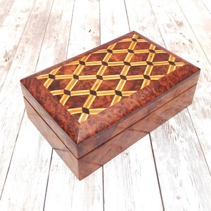 May include: A rectangular wooden box with a geometric inlaid design on the lid. The box is made of dark brown wood with a glossy finish. The lid features a pattern of interlocking diamonds in shades of brown, tan, and black.