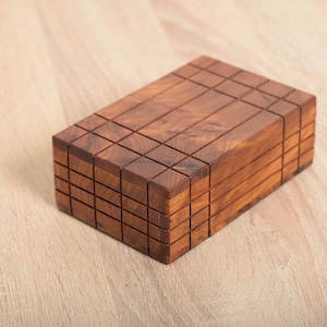 Peut inclure: Une boîte en bois avec un motif en grille sur le dessus et les côtés. La boîte est en bois foncé et a une finition naturelle.
